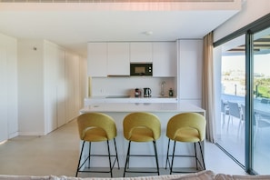 A modern kitchen with white cabinetry, a built-in microwave, and a bar area with three stools. - Premium penthouse with sea views (La Cala de Mijas)