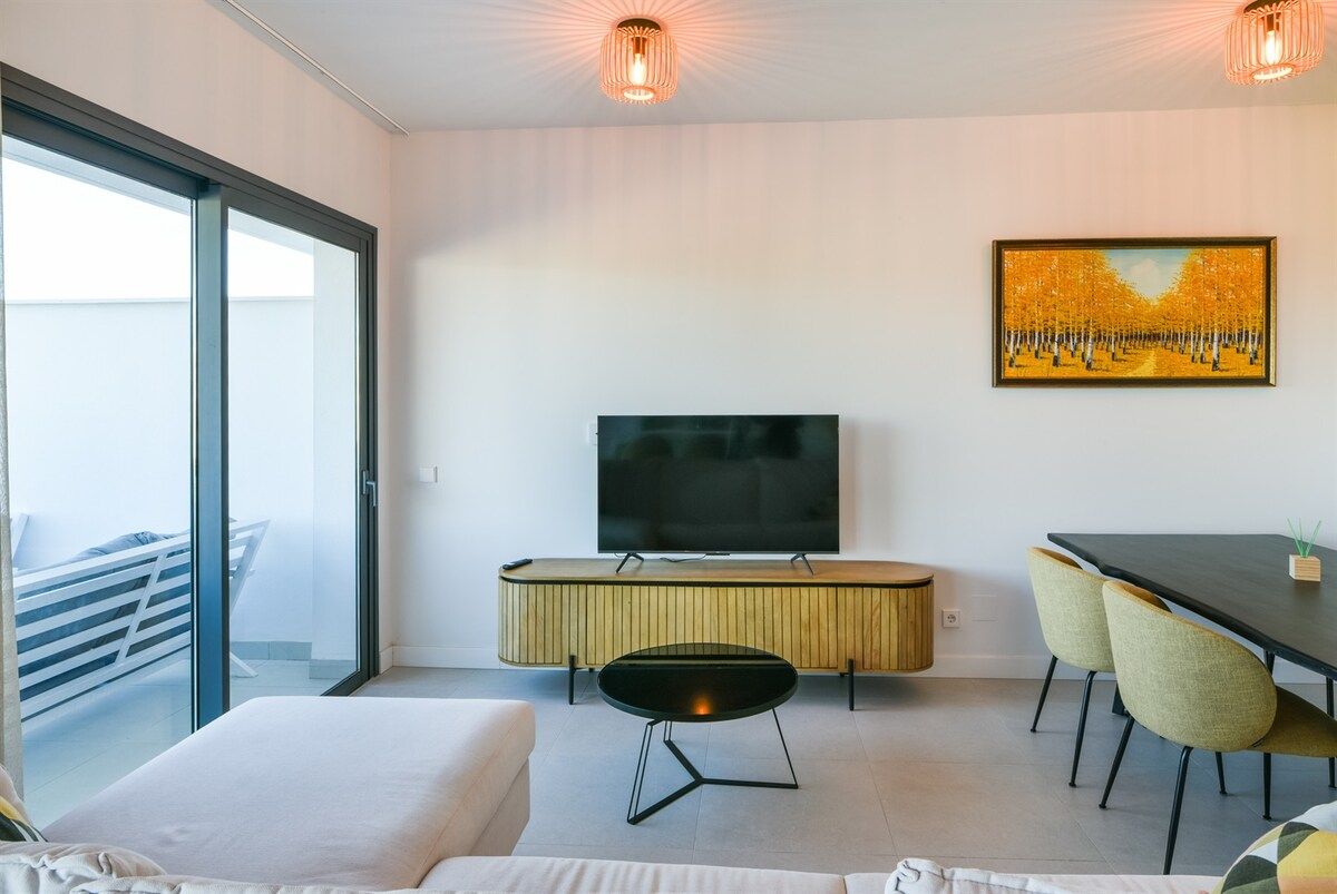 Une chambre d’hôtel moderne avec un grand lit, une télévision, une table à manger avec des chaises et un tableau au mur.
