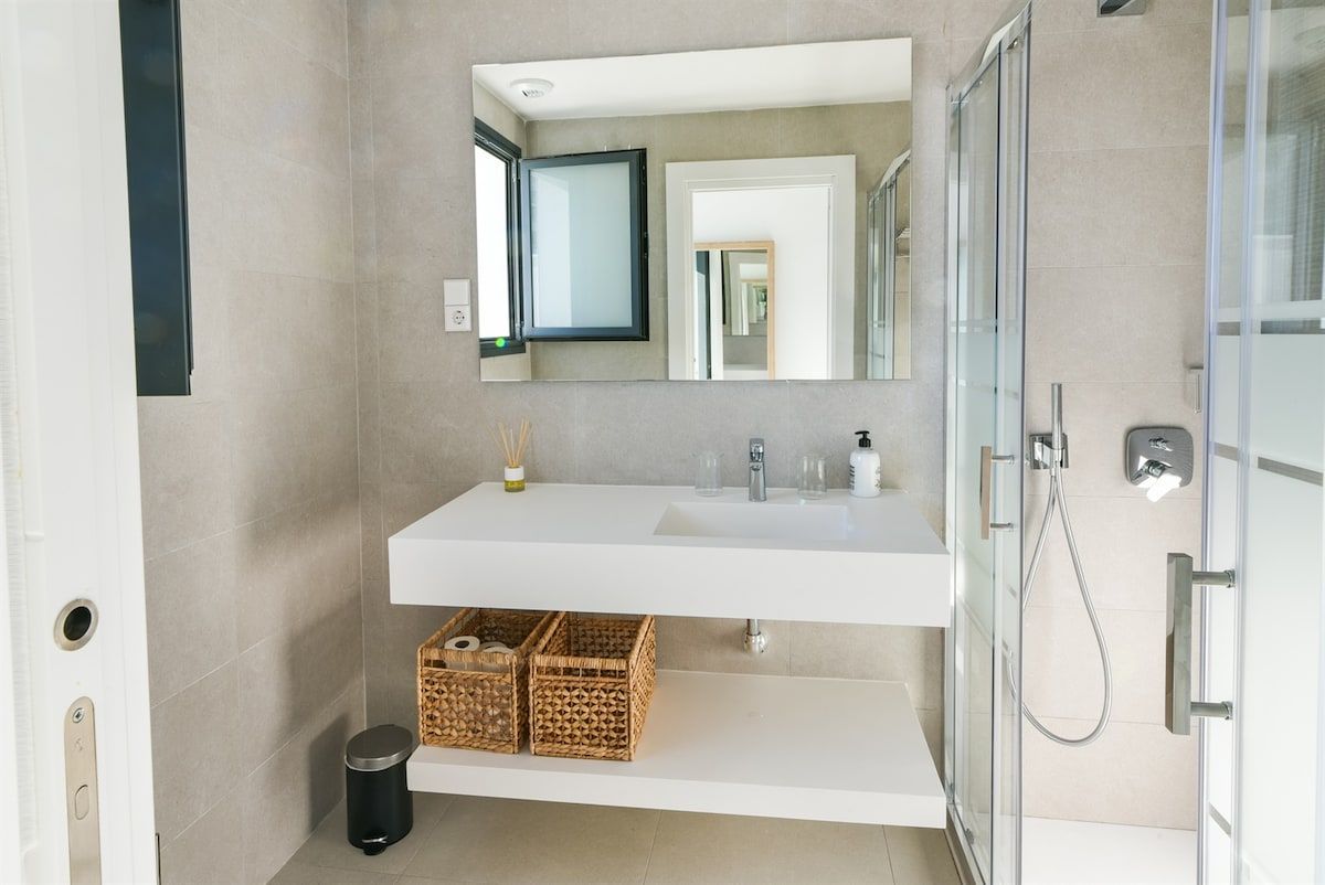 Ein modernes Badezimmer mit einem weißen Waschtisch, einem großen Spiegel und einer Glasdusche.