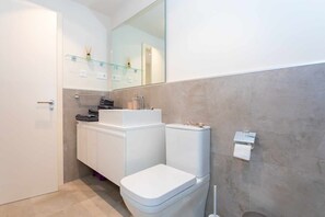 Een moderne badkamer met toilet, wastafel en spiegel.