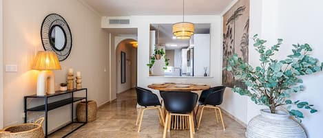 A hallway with a dining area featuring a round table, black chairs, and a hanging light fixture.