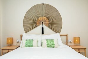 A bed with white bedding and green patterned pillows, flanked by two bedside tables with wicker lamps.