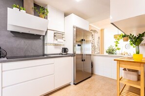 A modern kitchen with white cabinets, a stainless steel refrigerator, and a wooden table with a yellow bowl.