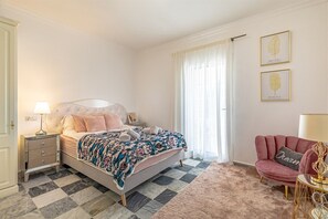 Ein Schlafzimmer mit einem Bett, einem Nachttisch, einem Sessel und einem Fenster mit Vorhängen.