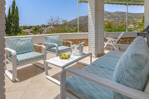 Eine Terrasse mit weißen Möbeln, einem Tisch mit Obstschale und Blick auf die Landschaft.