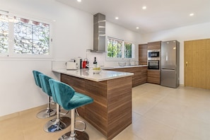 A modern kitchen with a central island, bar stools, and built-in appliances. - Luxury villa with private tennis & heated pool (Mijas)