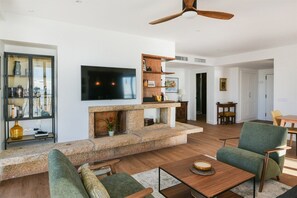 A modern living room with a stone fireplace, a flat-screen TV, and a ceiling fan.