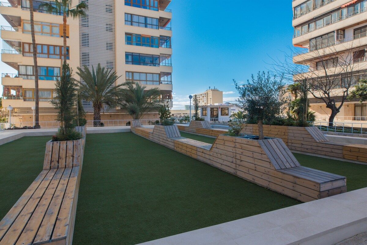 A courtyard with artificial grass, wooden benches, and palm trees.