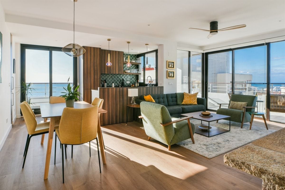 A modern living room with a dining area, a sofa set, and a kitchen area with a view of the sea.