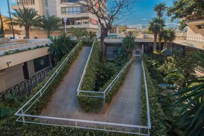A rooftop garden with a pathway, surrounded by greenery and palm trees.