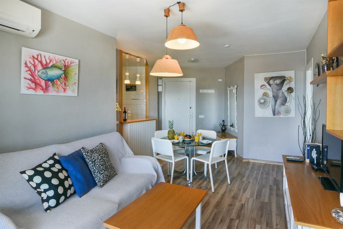 Ein modernes Wohnzimmer mit einer Couch, einem Esstisch mit Stühlen und einer Küchenzeile mit Kühlschrank.
