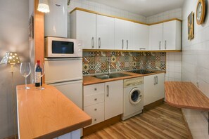 Eine kompakte Küche mit weißen Schränken, einer Mikrowelle, einer Waschmaschine und einer dekorativen Spritzschutzwand.