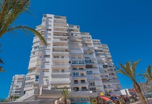 Un hotel de varios pisos con balcones, piscina y palmeras.