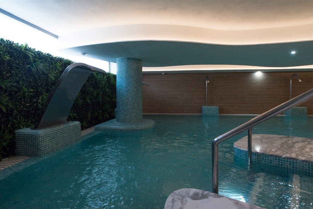 Une piscine intérieure avec un sol carrelé, un bord en marbre et une rampe métallique.