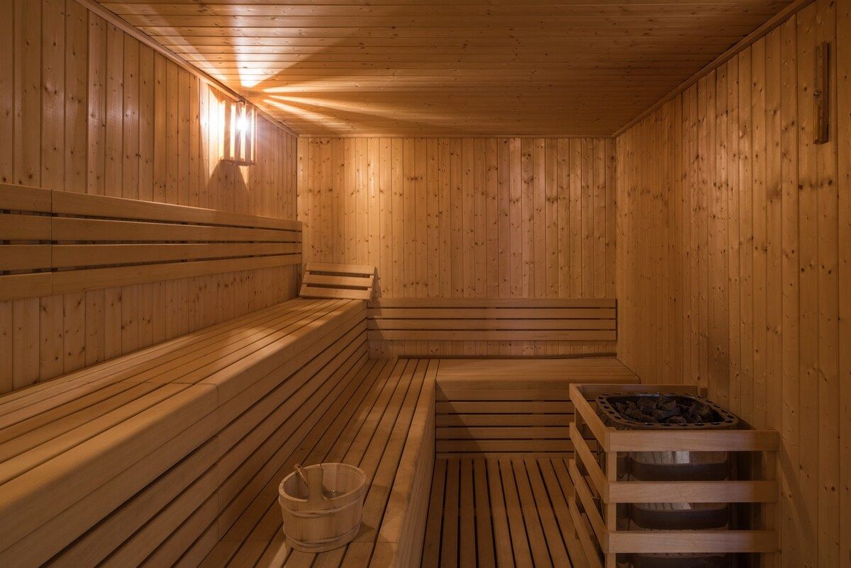 Una sauna con bancos de madera y suelo de madera, un balde y un calentador de sauna.
