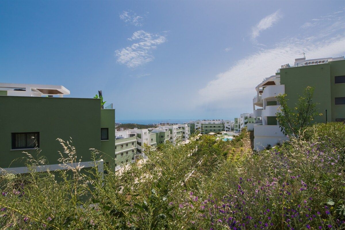 A residential area with modern buildings, a clear sky, and a view of the sea.