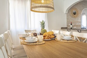 A dining area with a wooden table set for breakfast, including croissants, a pineapple, and coffee cups. - Luxury villa, heated pool. 3 min walk to beach (Marbella)