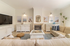 A living room with a television, white cabinets, a fireplace, framed pictures, and a beige sofa.