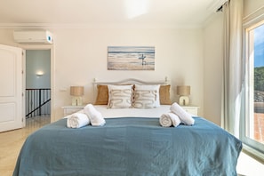 Ein Schlafzimmer mit einem großen Bett, einem Gemälde von einer Strandansicht und einem Fenster mit Blick.