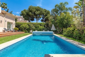 A swimming pool with a clear blue water, surrounded by a well-maintained lawn and various trees. - Luxury villa, heated pool. 3 min walk to beach (Marbella)