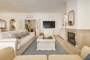 Ein Wohnzimmer mit einem weißen Sofa, einem Glastisch, einem Kamin und einem Fernseher.
