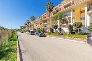 A multi-story hotel with balconies, parked cars, and palm trees.