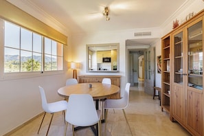 A dining area with a round table and white chairs, a kitchen in the background, and a view of the outdoors. - Beautiful views from 2 terraces with pool &parking (Mijas Golf)