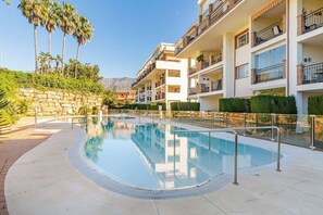 A swimming pool surrounded by a stone wall, with a multi-story building in the background. - Beautiful views from 2 terraces with pool &parking (Mijas Golf)