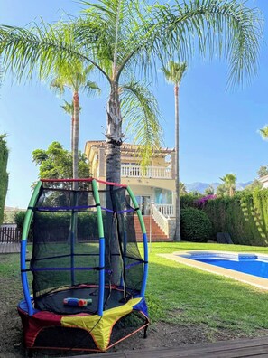 A trampoline set up in a backyard with a pool and palm trees. - Villa, heated pool, golf, games, BBQ! (Mijas Golf)