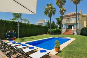 A swimming pool with lounge chairs, palm trees, and a two-story building with a balcony.