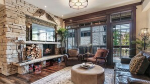 A cozy living room with a stone fireplace, leather sofas, and a large TV.