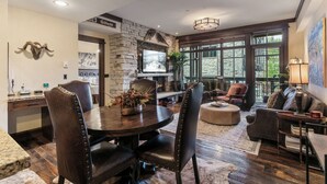 A spacious living area with a stone fireplace, leather furniture, and large windows offering a view of the outdoors.
