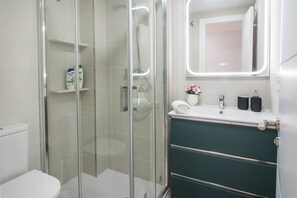 Un baño moderno con ducha envuelta en vidrio, inodoro blanco, tocador con espejo y un mueble de almacenamiento verde.