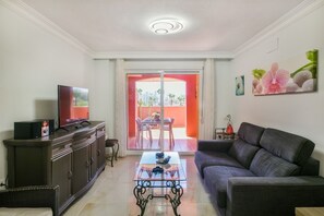 A living room with a sofa, a coffee table, a TV on a cabinet, and a dining area with a table and chairs.
