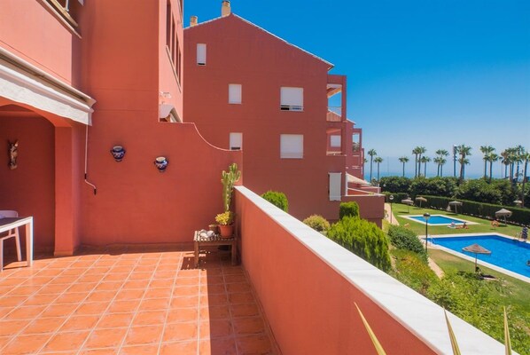 A red building with a tiled patio, a pool, and palm trees in the background.