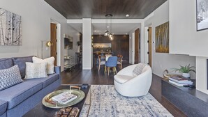 A modern living room with a sofa, armchair, and coffee table. There is a dining area with chairs and a table in the background. - One Empire Pass Lodge at Deer Valley Resort - Two Bedroom Residence #105 2 Condo (Park City)