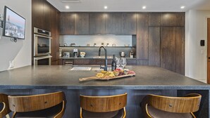 A modern kitchen with dark wood cabinets, a central island with bar stools, and a variety of appliances including a refrigerator, oven, and coffee maker. - One Empire Pass Lodge at Deer Valley Resort - Two Bedroom Residence #105 2 Condo (Park City)