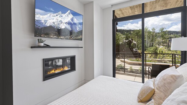 A modern bedroom with a large TV, fireplace, and a balcony with a scenic view. - One Empire Pass Lodge at Deer Valley Resort - Two Bedroom Residence #105 2 Condo (Park City)