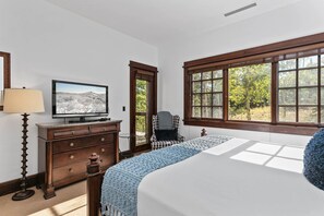 Un dormitorio con cama, cómoda, televisor, una silla y ventanas amplias.