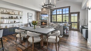 A spacious living area with a fireplace, a dining table with chairs, and a large window offering a view of the outdoors.