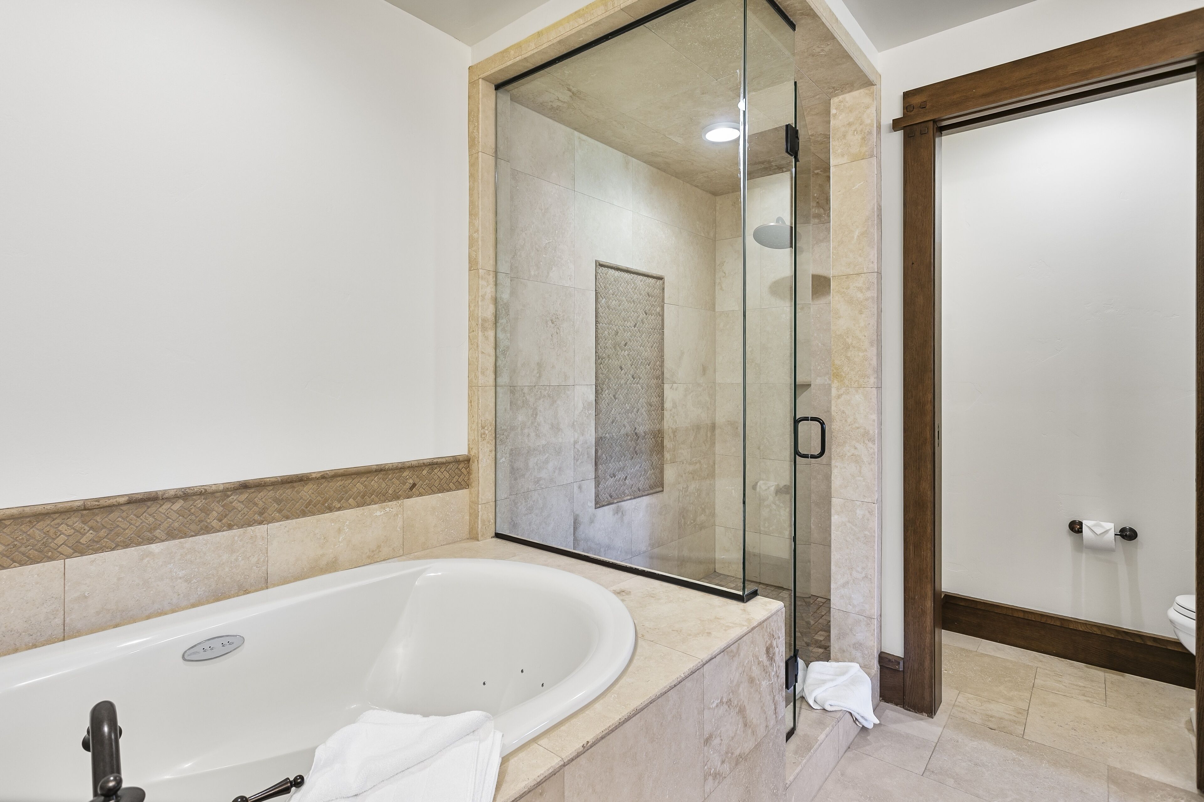 Un baño moderno con una bañera independiente, cabina de ducha con paredes de vidrio y una puerta de madera.