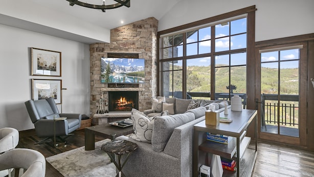 A cozy living room with a stone fireplace, comfortable seating, and a large window offering a scenic view.