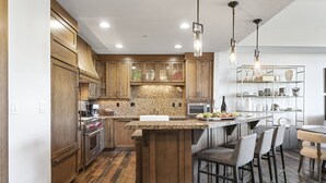 A kitchen with wooden cabinets, granite countertops, a central island with bar stools, and pendant lighting.