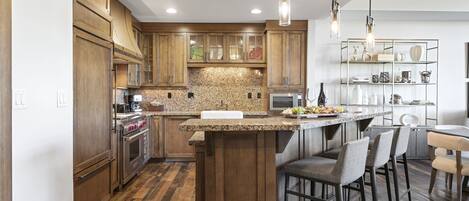 A kitchen with wooden cabinets, granite countertops, a central island with bar stools, and pendant lighting.