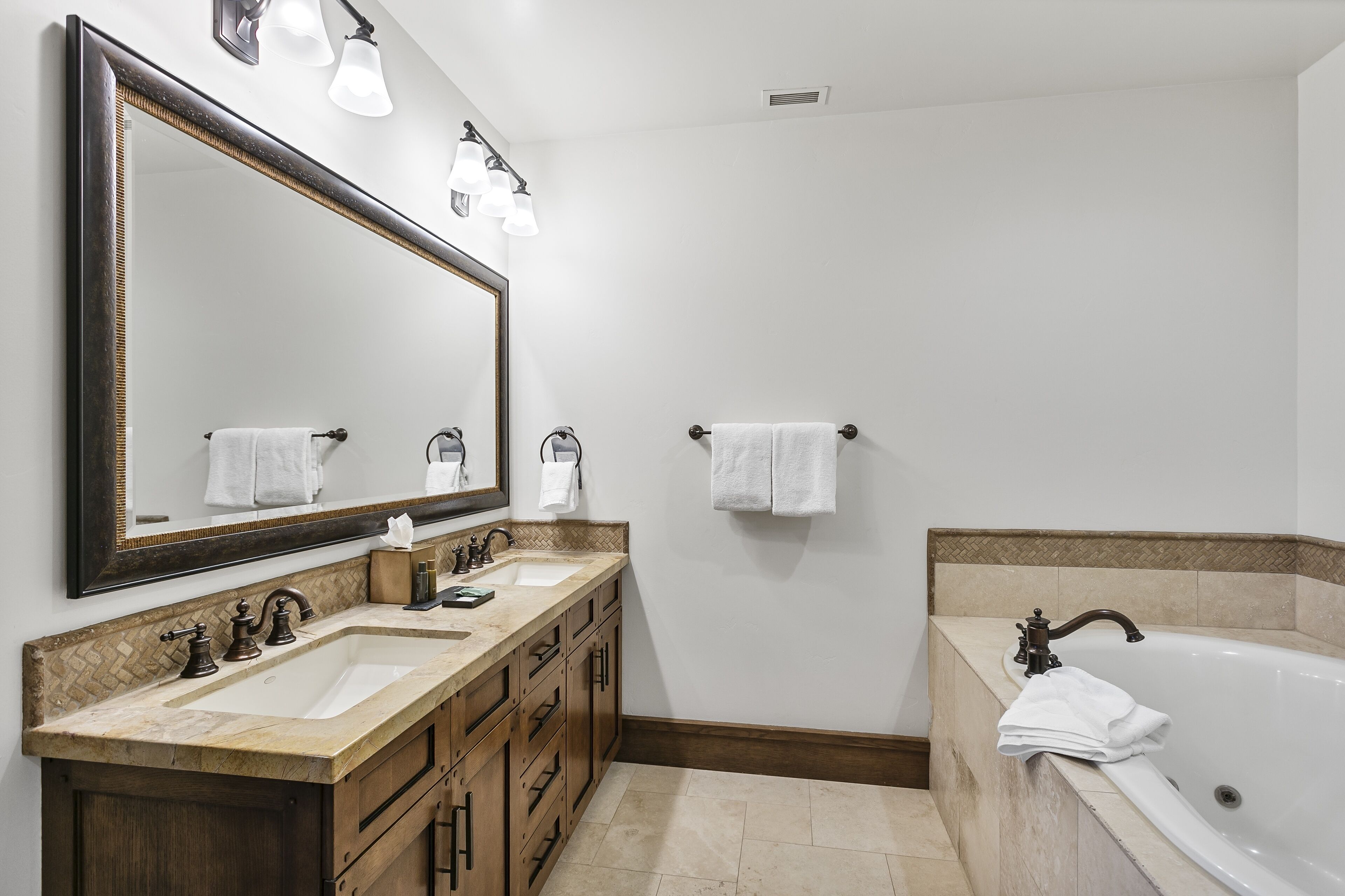 Un baño con tocador doble, un espejo grande, una bañera y dos toalleros.