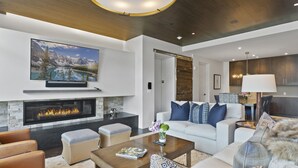 Un salon moderne avec une cheminée, un grand téléviseur à écran plat, un canapé agrémenté de coussins à motifs et une table basse.