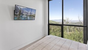 Une chambre avec une grande fenêtre, un lit et un tableau représentant un paysage de montagne.