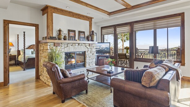 A spacious living room with a stone fireplace, leather sofas, and a large window offering a view of the outdoors. - Shooting Star Lodge at Deer Valley Resort - Two Bedroom Residence #203 2 Condo (Park City)