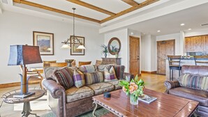 A spacious living room with a wooden ceiling, a leather sofa, a coffee table, and a dining area with wooden cabinets. - Shooting Star Lodge at Deer Valley Resort - Two Bedroom Residence #203 2 Condo (Park City)