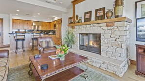 A spacious living area with a stone fireplace, wooden ceiling beams, and a kitchen in the background. - Shooting Star Lodge at Deer Valley Resort - Two Bedroom Residence #203 2 Condo (Park City)